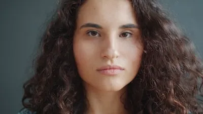 Retrato de Camila Duarte, cabelos escuros e cacheados, sobre fundo escuro