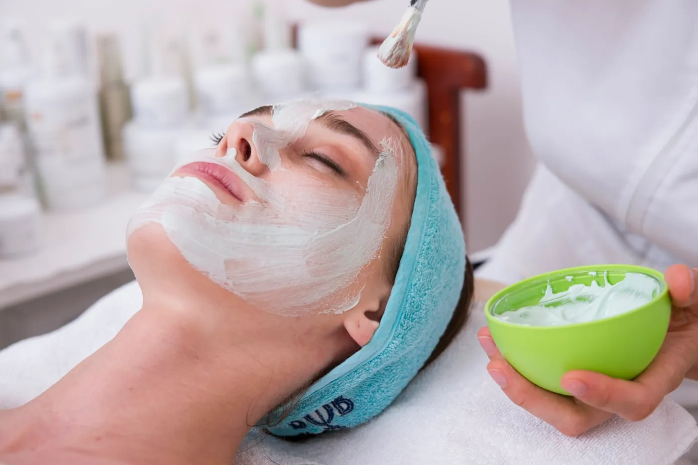 Profissional aplicando máscara facial branca em uma cliente deitada