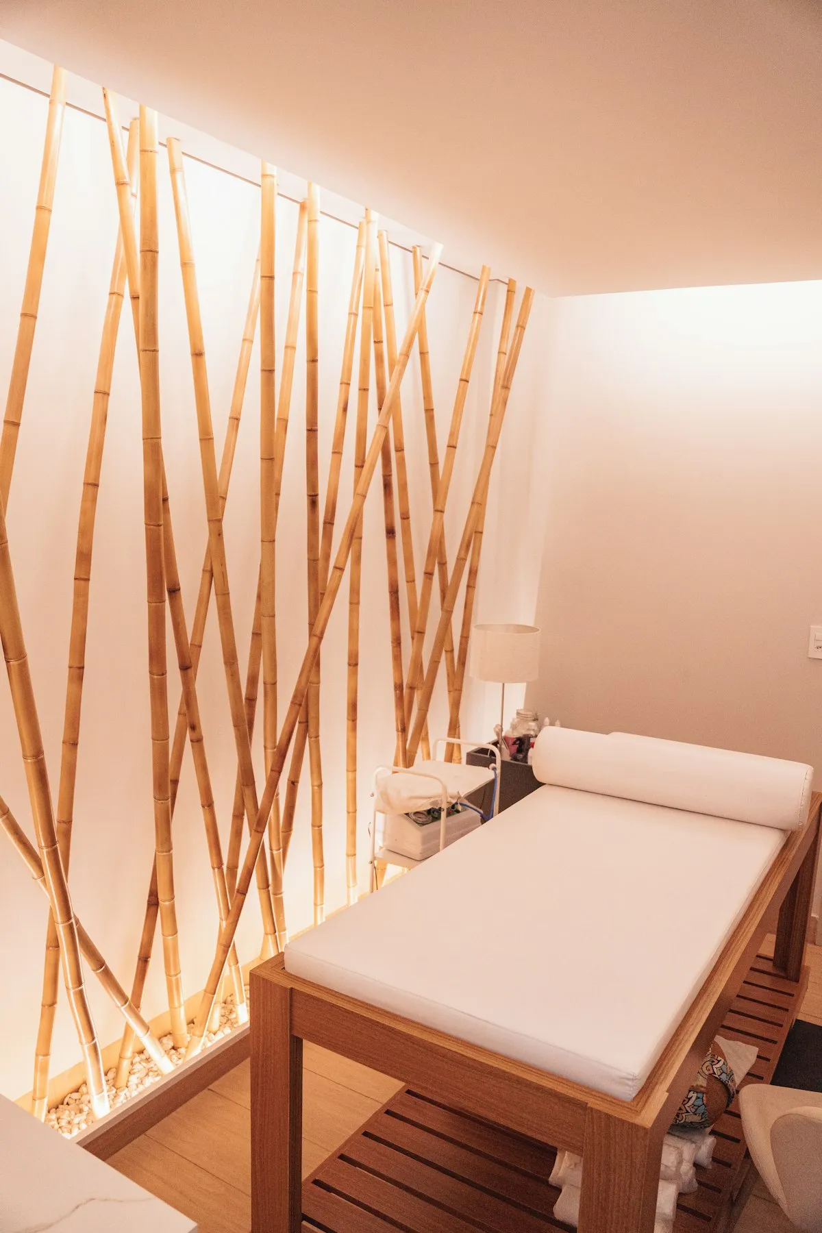 Sala de tratamento com maca branca, piso de madeira e painel de bambu retroiluminado