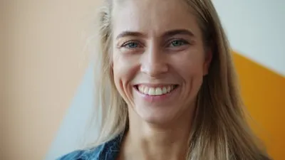 Retrato de Marina Oliveira sorrindo, cabelos loiros e fundo colorido